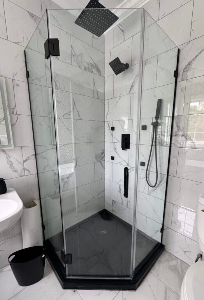 Glass corner shower enclosure featuring matte black fixtures, a rain showerhead, and white marble tile walls