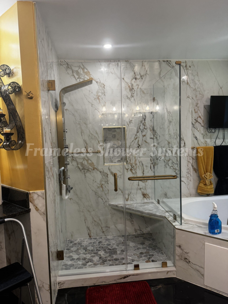 Frameless glass shower enclosure with brushed gold fixtures, marble tiled walls, corner bench, and hexagon floor tile