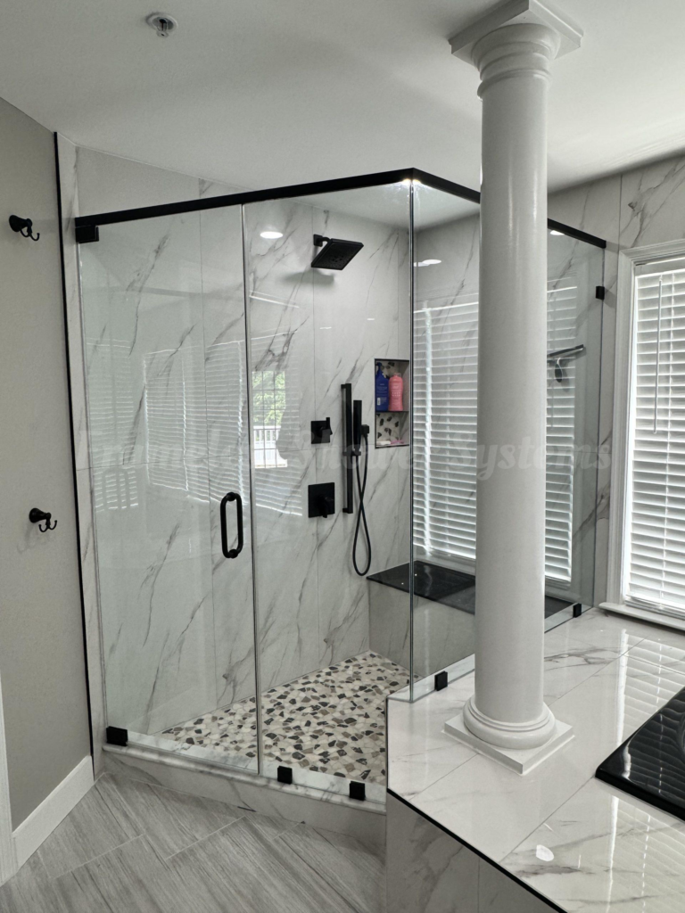 Modern glass shower enclosure with matte black hardware, marble walls, pebble tile floor, and an architectural column
