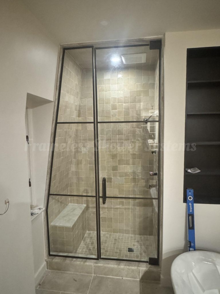 Glass shower enclosure with black metal grid frame, built-in tiled bench, and beige square tile walls