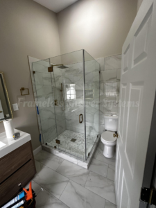 Modern bathroom with a frameless glass shower enclosure, brass fixtures, and marble-look tile walls