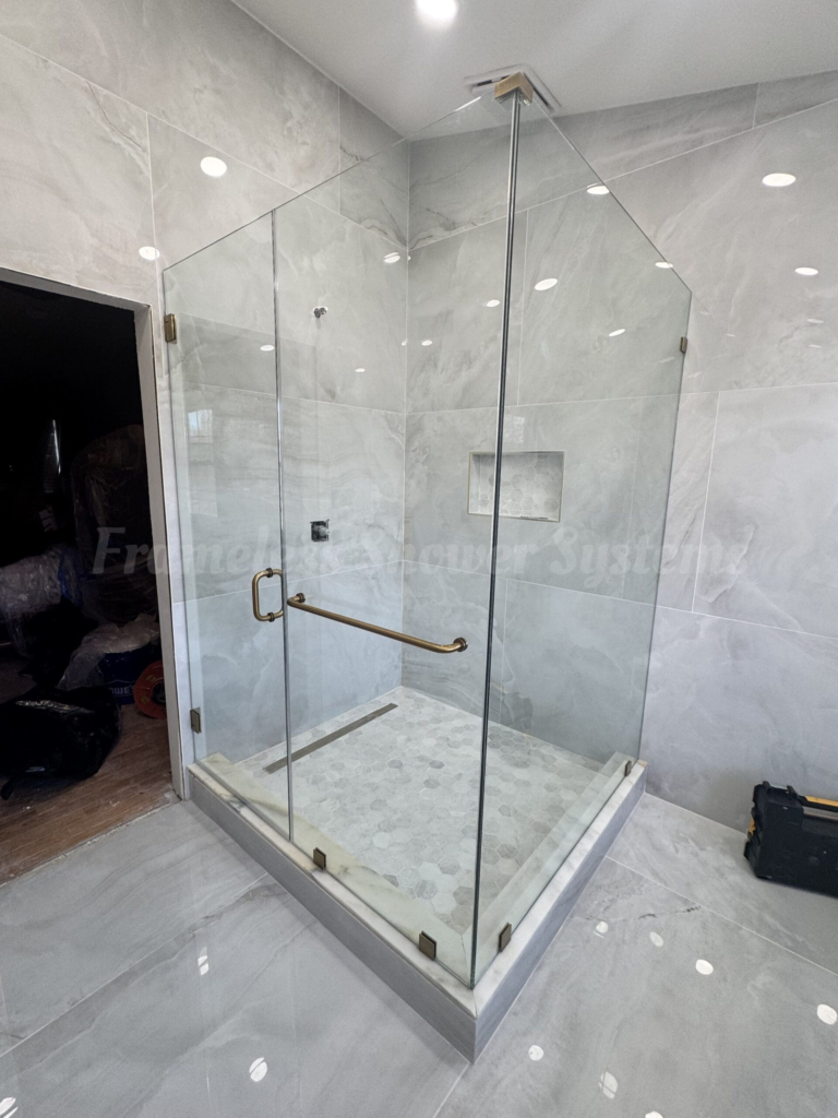 Modern frameless glass shower enclosure with brass hardware, light marble wall tiles, and hexagonal floor tiles