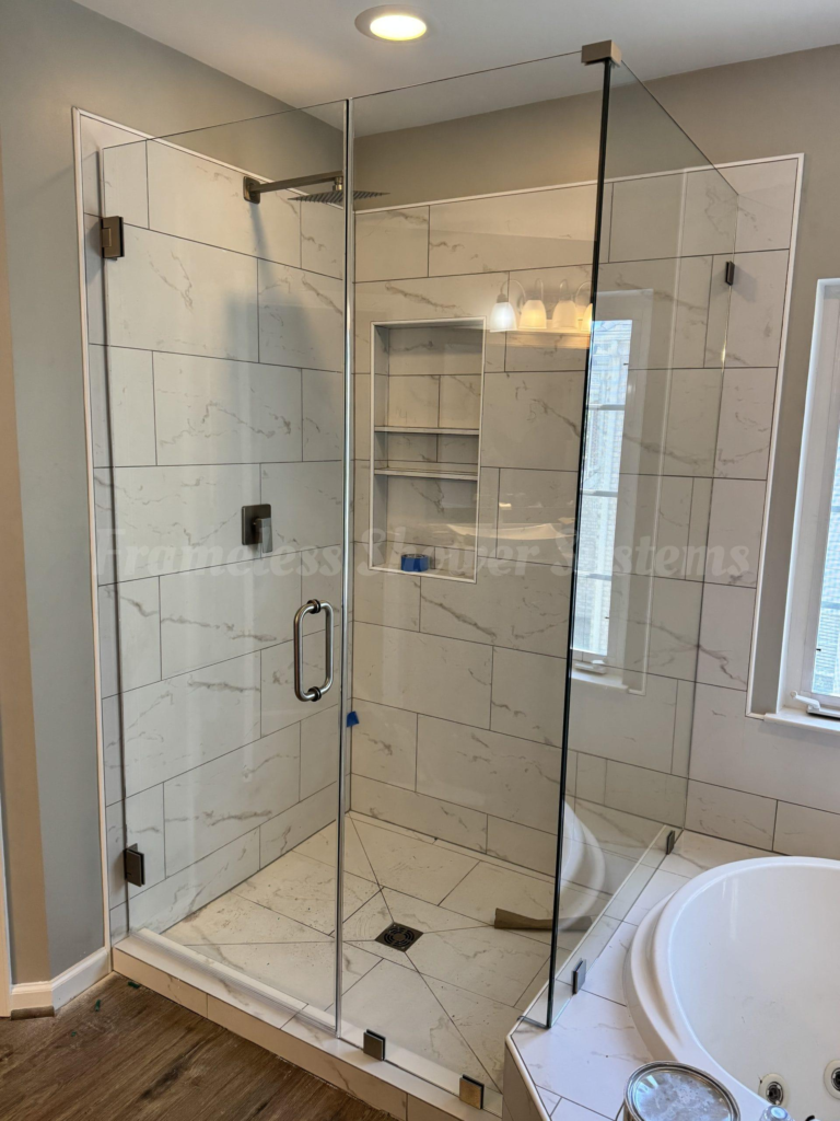 Frameless glass shower enclosure featuring marble-patterned wall tile, brushed metal hardware, and a built-in shelf niche