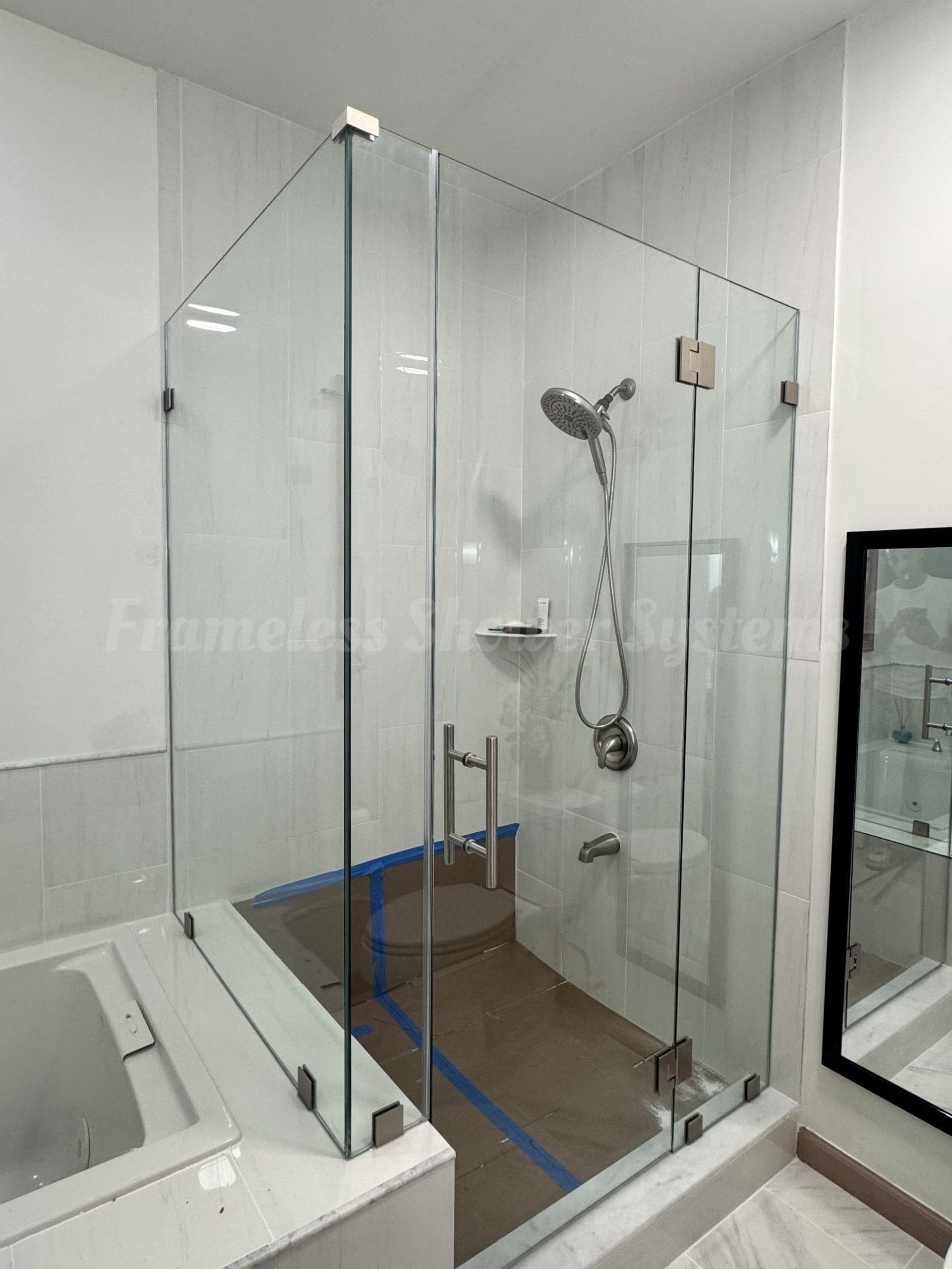 Frameless glass shower enclosure with brushed metal hardware in a modern white tiled bathroom