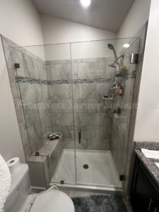 Frameless glass shower enclosure featuring gray tile walls, a built-in bench, and chrome hardware