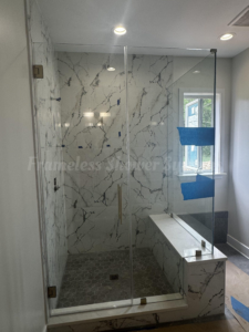 Modern frameless glass shower enclosure with marble-patterned wall tile, hexagonal floor tile, and a built-in bench