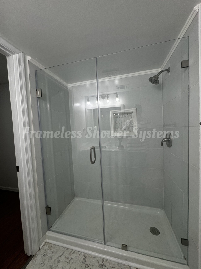 Frameless glass shower enclosure with a hinged door, brushed metal hardware, and tiled walls
