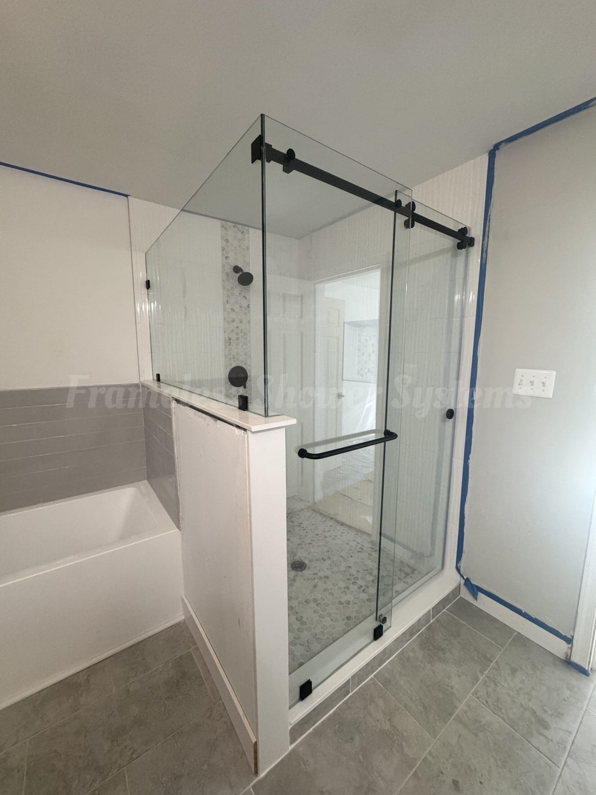 Frameless glass shower enclosure with matte black sliding hardware mounted on a half wall next to a bathtub