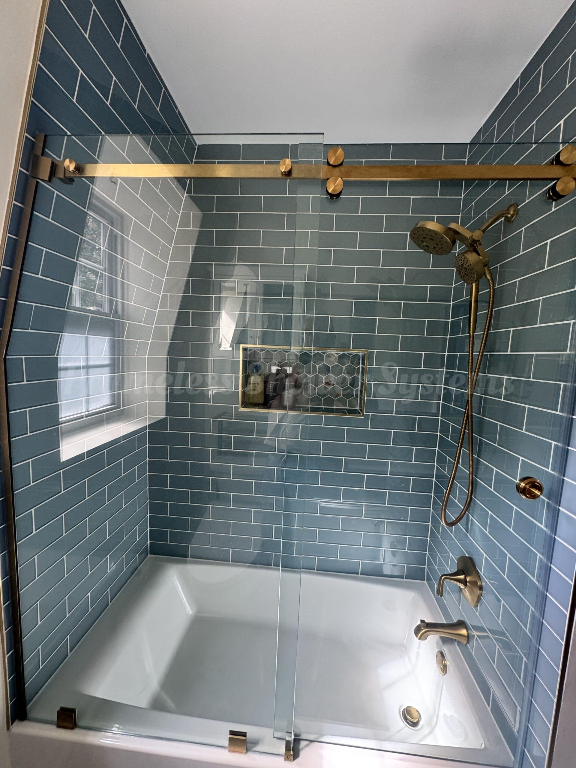 Modern shower and tub with blue subway tile, brushed brass fixtures, sliding glass doors, and a recessed niche