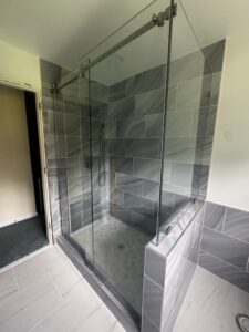 Walk-in shower with frameless sliding glass doors, grey marble-look wall tiles, and hexagon floor tile