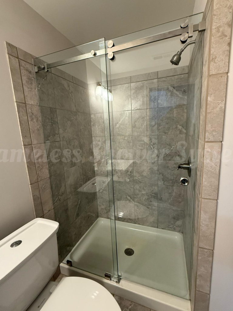 Frameless sliding glass shower enclosure with grey tile walls and brushed nickel hardware