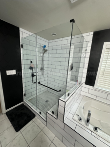 Frameless glass shower enclosure with black hardware, white subway tile, and hexagonal floor tile next to a bathtub
