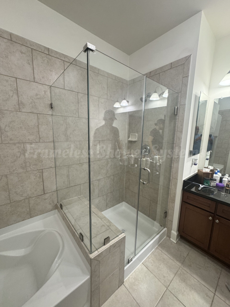 Frameless glass shower enclosure with beige tiled walls and chrome hardware next to a bathtub