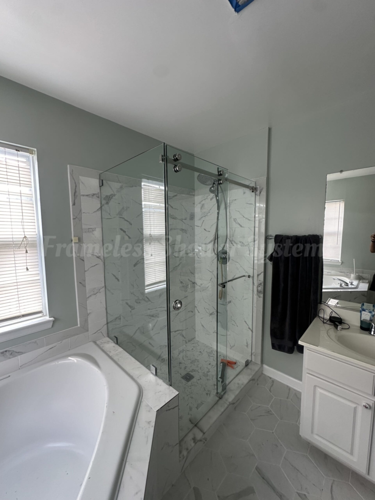 Frameless glass shower enclosure with marble tile walls next to a white bathtub in a modern bathroom