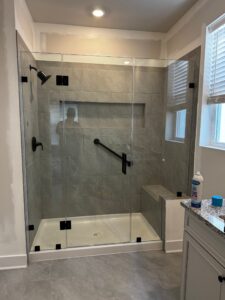 Modern walk-in shower with frameless glass enclosure, grey tile walls, built-in bench, and matte black fixtures