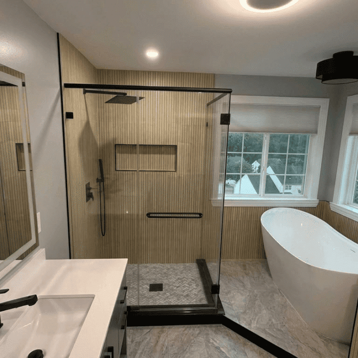 Modern bathroom with a glass walk-in shower, freestanding white bathtub by windows, and vanity with black fixtures