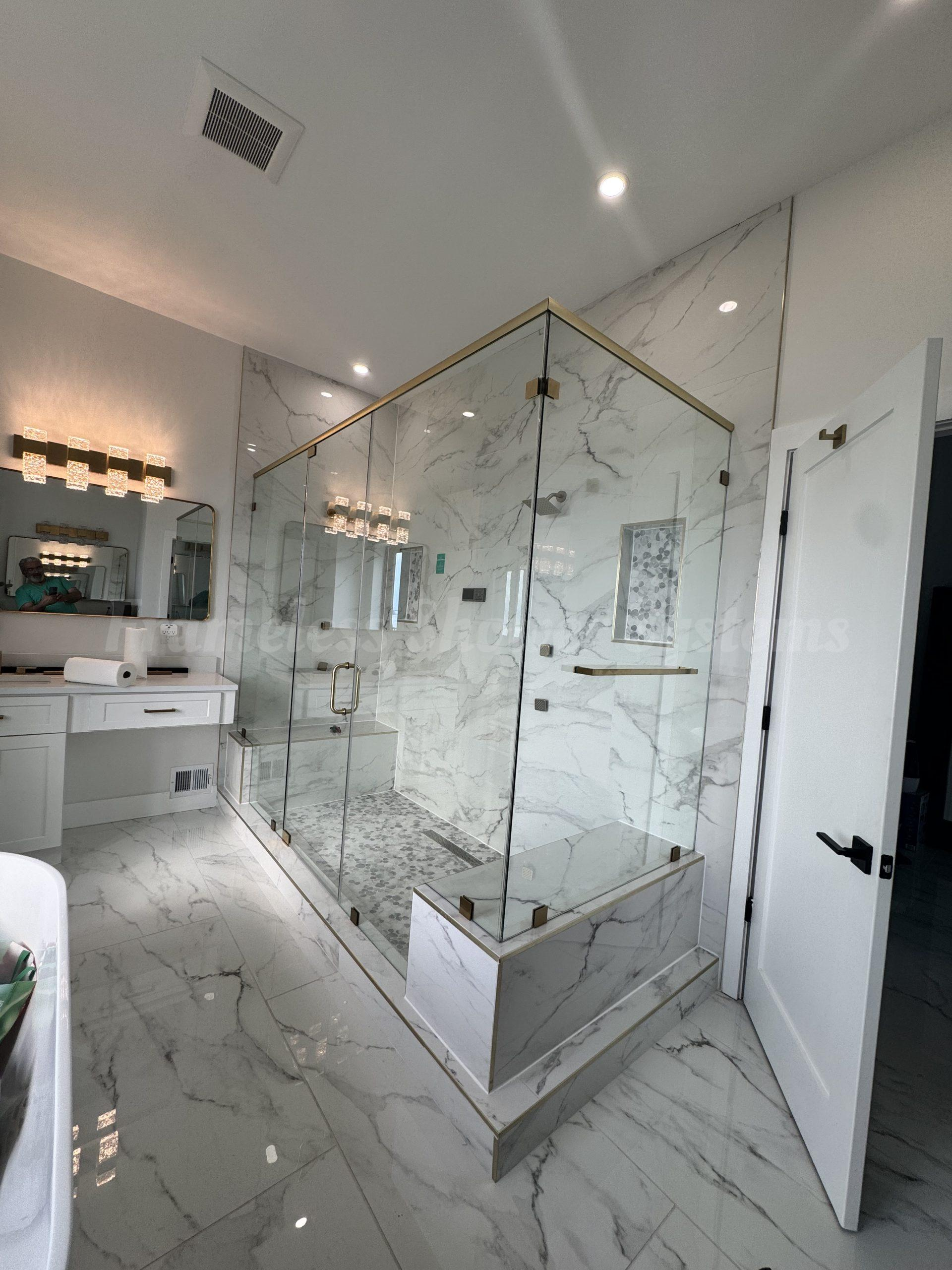 Modern bathroom featuring a glass walk-in shower enclosure with gold hardware and marble tile walls