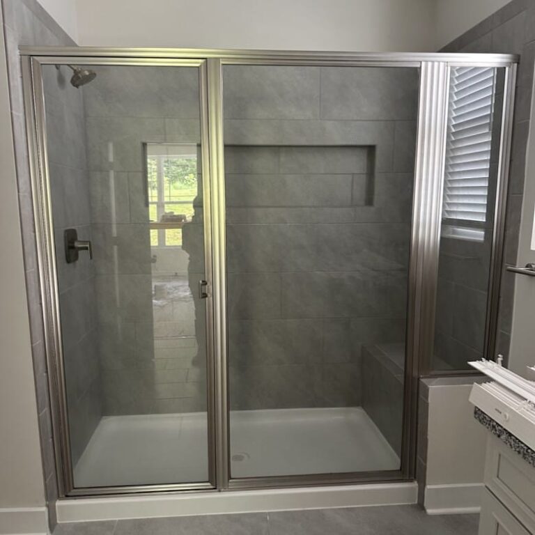 Walk-in shower with brushed nickel framed glass doors, grey tile walls, built-in bench, and recessed wall niche