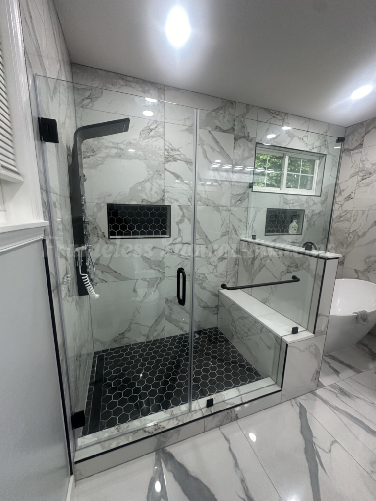 Modern walk-in glass shower with white marble walls, black hexagonal floor tile, built-in bench, and matte black fixtures