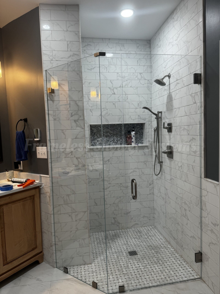 Frameless glass walk-in shower with white marble subway tile walls, mosaic tile floor, and a recessed tiled niche