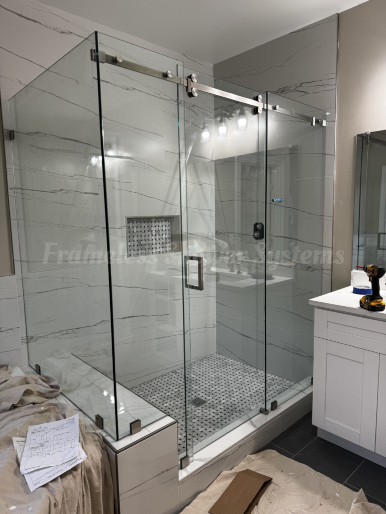 Frameless glass sliding shower enclosure with brushed metal hardware and marble-style tiled walls