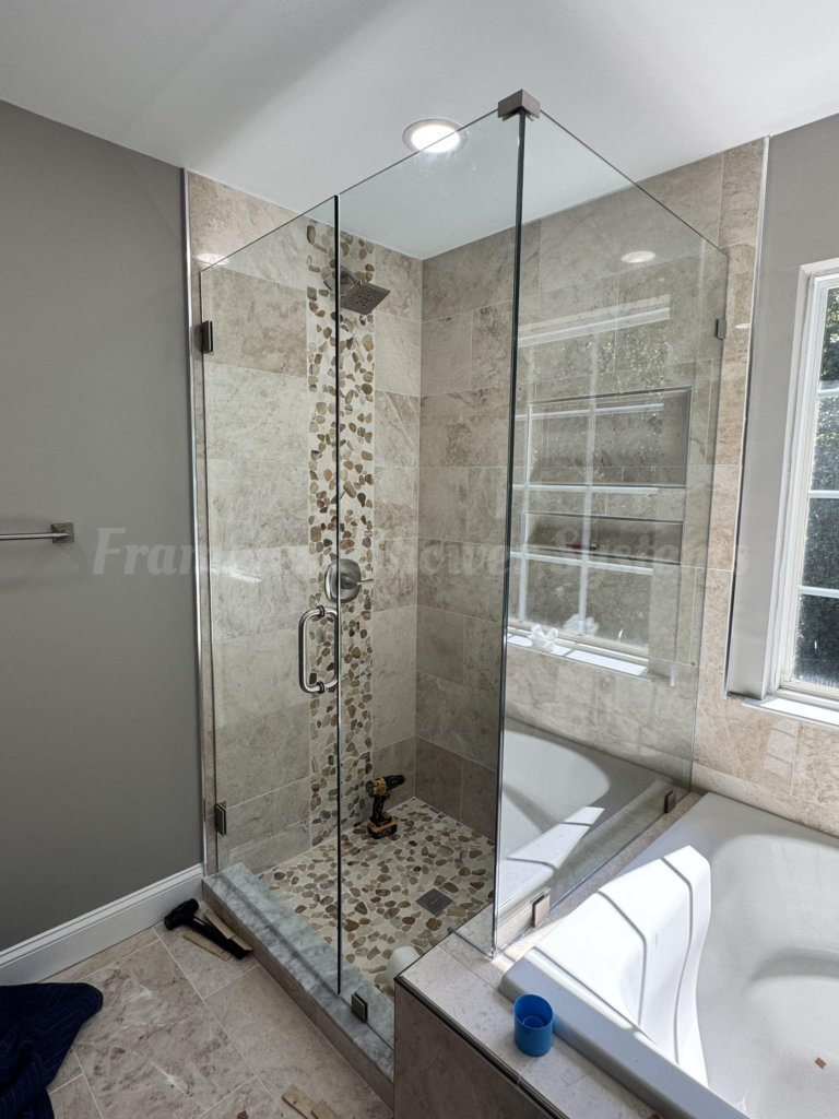 Frameless glass shower enclosure with beige stone tiles, vertical pebble accent strip, and pebble floor next to a bathtub