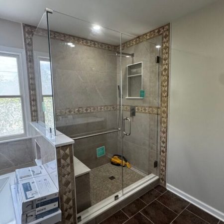 Walk-in shower featuring frameless glass enclosure, beige wall tiles with patterned accent trim, and a built-in bench