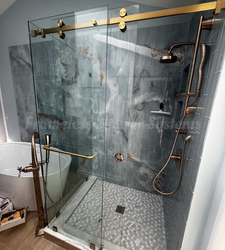 Frameless sliding glass shower enclosure with brushed brass hardware, blue marble wall tiles, and an adjacent freestanding bathtub